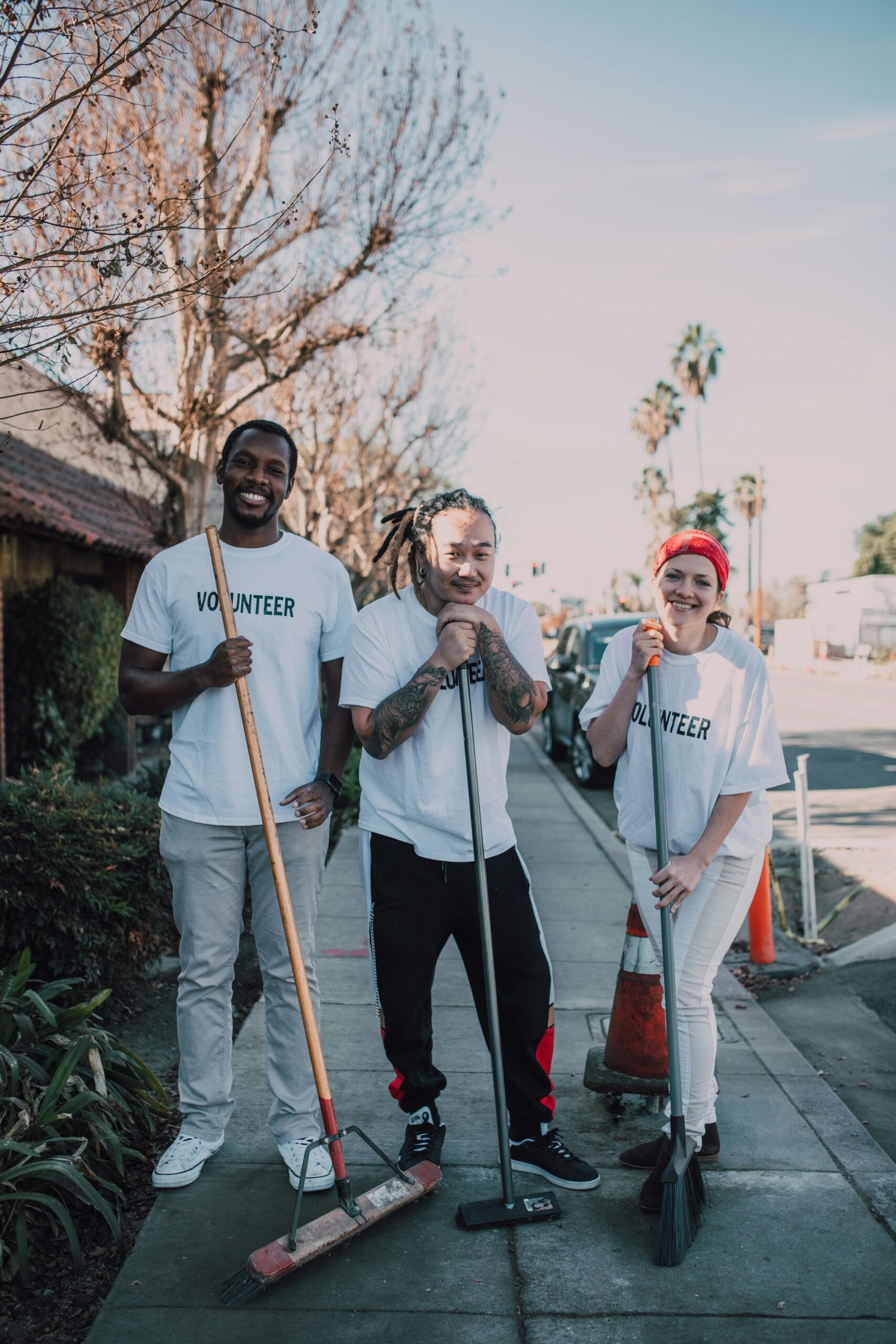 A group of cheerful volunteers cleaning a sidewalk on a sunny day, promoting community service.